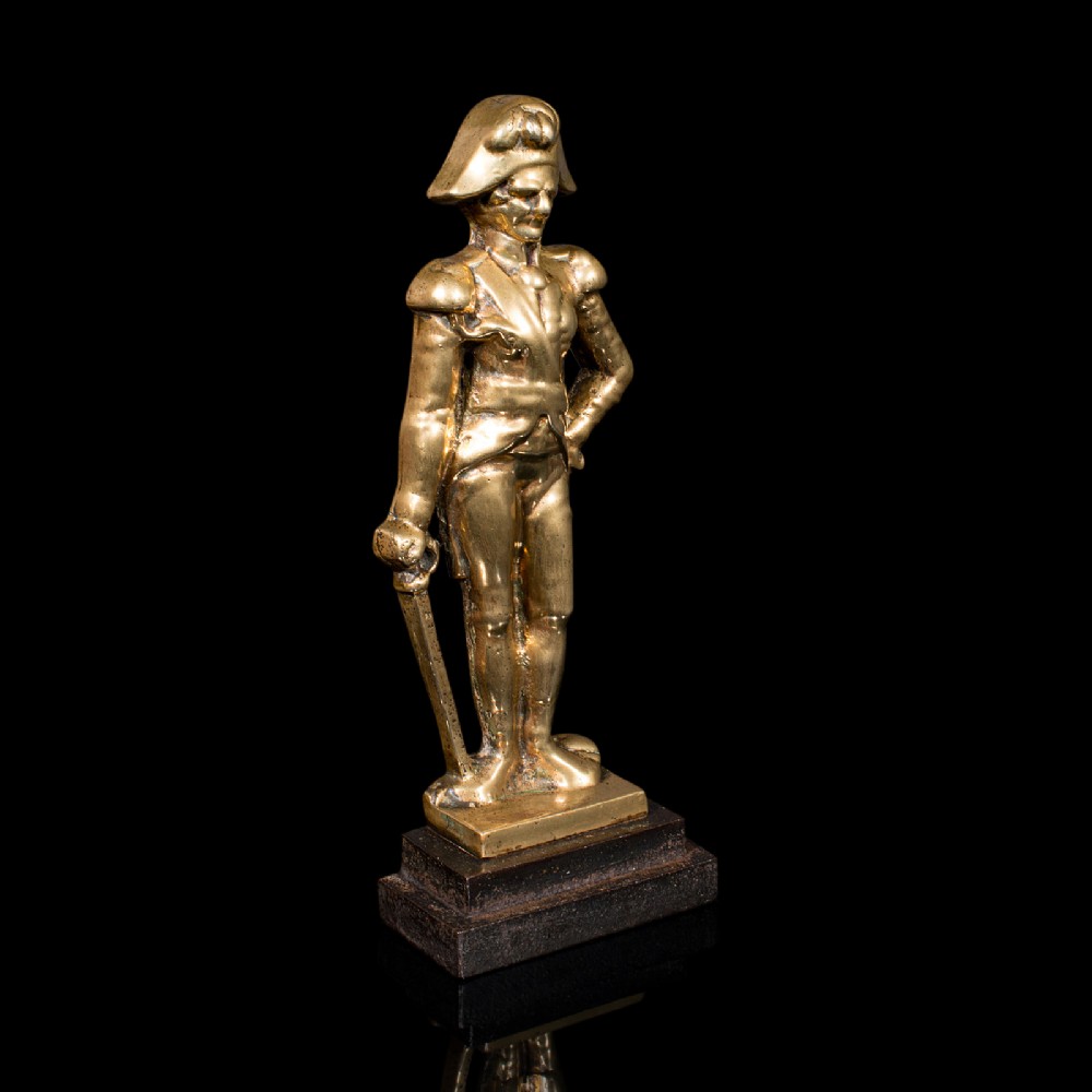 A late Georgian brass figural doorstop depicting Admiral Lord Nelson standing in military attire upon a dark stepped base.