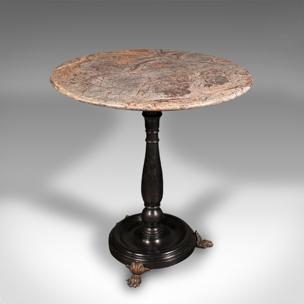 A circular veined marble top resting upon a dark turned wooden pedestal stem with a round plinth base and three brass claw feet.