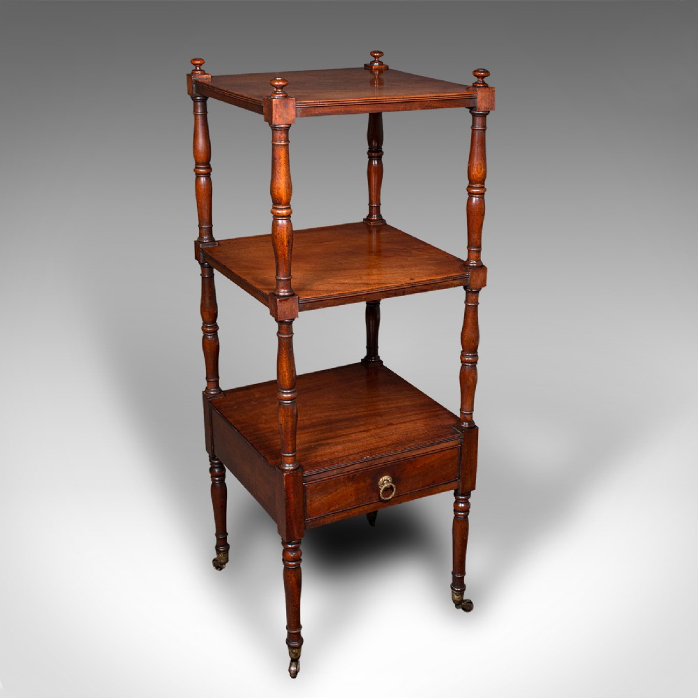 A three-tier Late Georgian mahogany whatnot featuring turned upright supports, finials, a lower drawer with a brass ring handle, and brass castors.