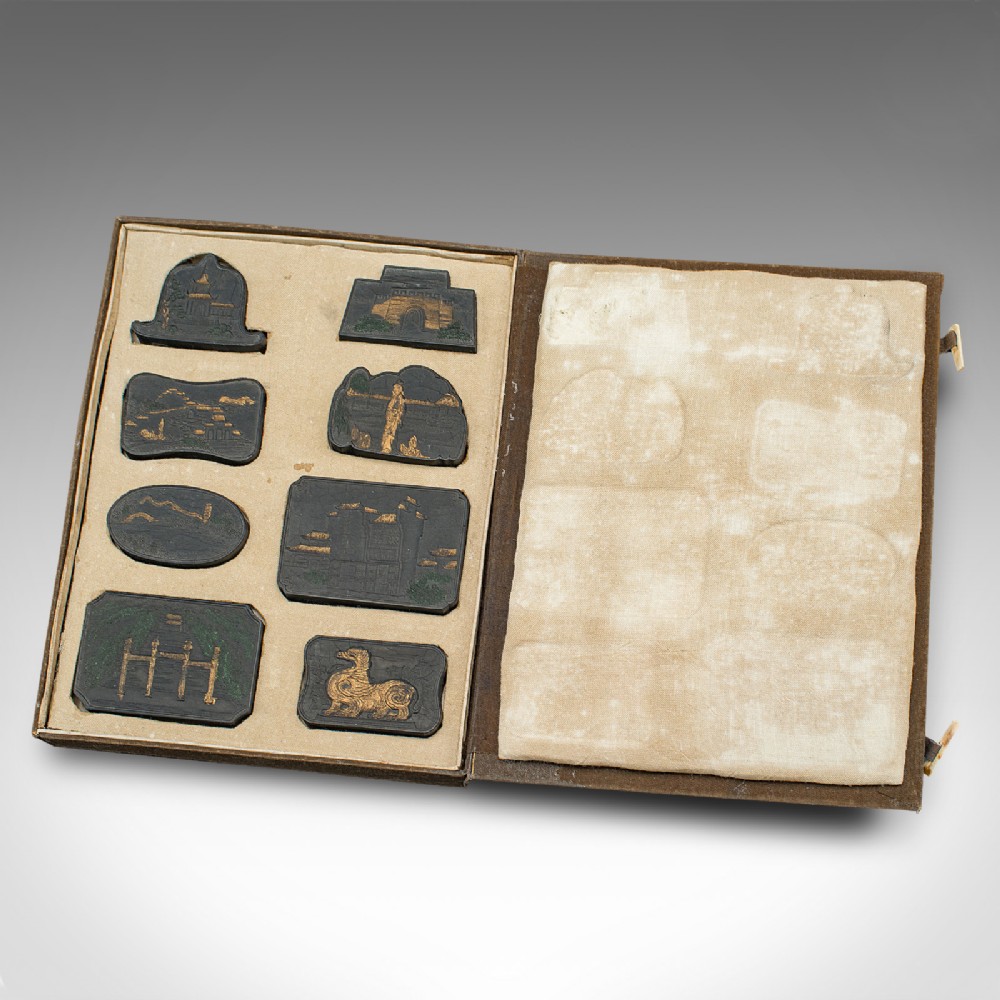 An open fabric-lined box displaying a set of eight black Chinese ink blocks adorned with gold and green moulded architectural and figural motifs.