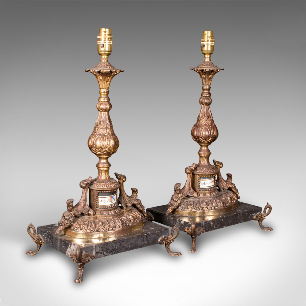 A pair of ornate French gilt metal table lamp bases mounted on black veined marble plinths with scrolled feet.