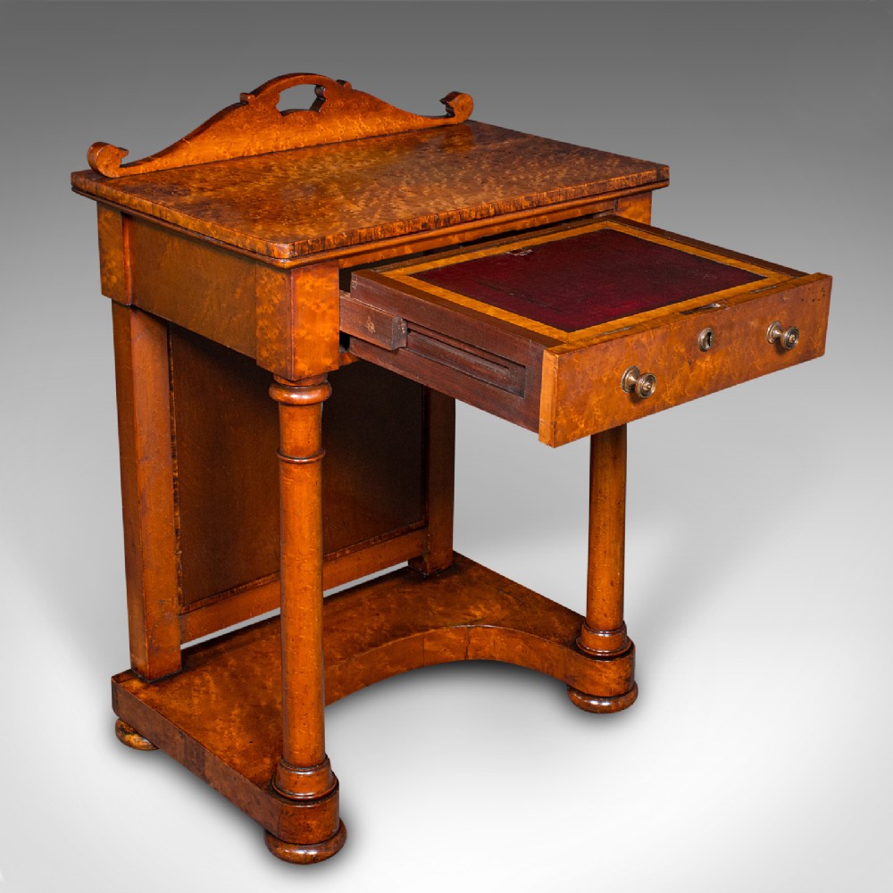 An antique burr maple writing desk featuring a scrolled back gallery, a pull-out drawer with a red leather inset skiver, turned column supports, and a shaped plinth base.