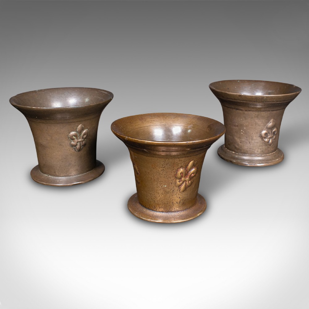 A set of three English antique cast bronze apothecary mortars featuring flared rims, circular bases, and raised fleur-de-lis motifs.