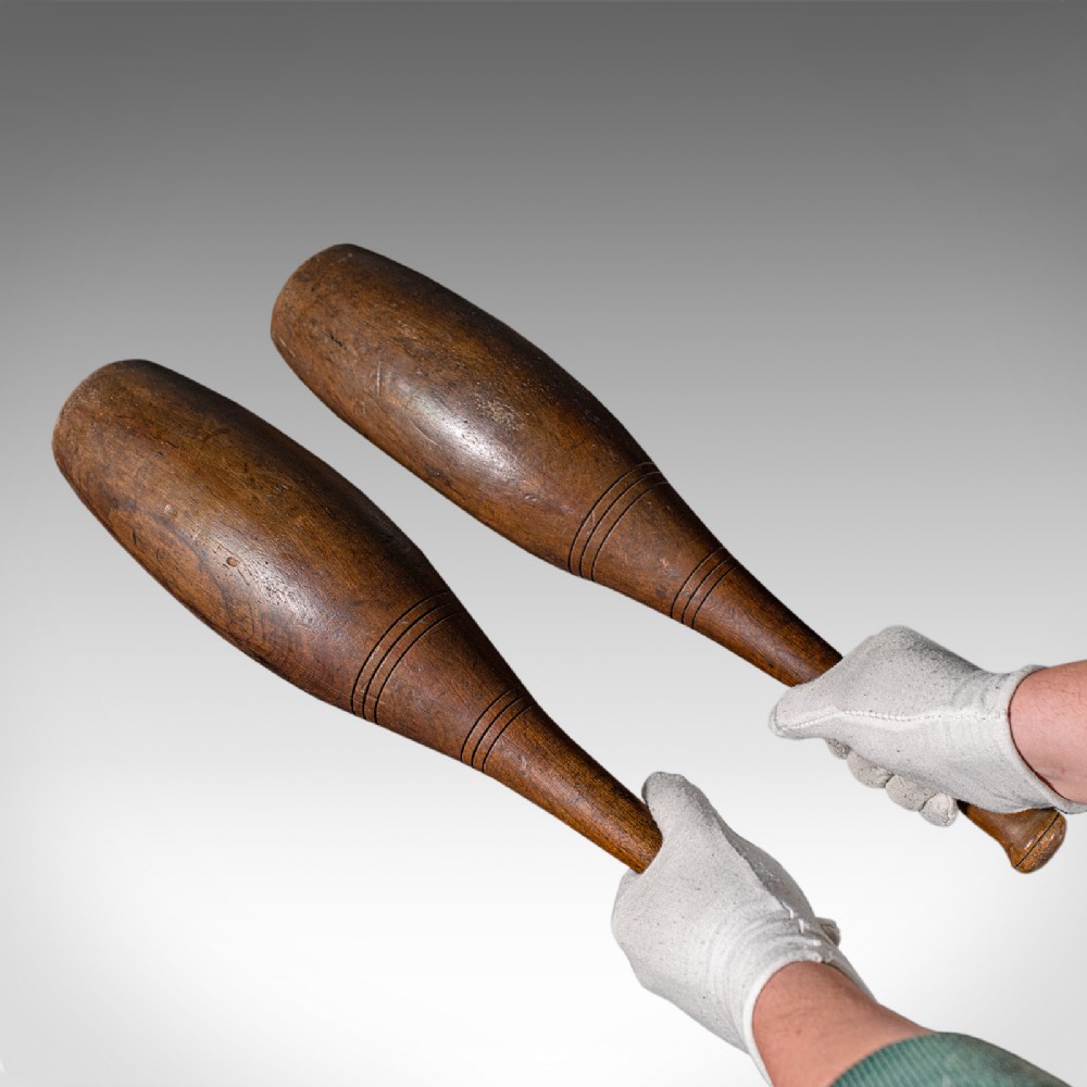 A pair of turned brown beech wood Indian exercise clubs featuring incised decorative ring grooves on the handles.