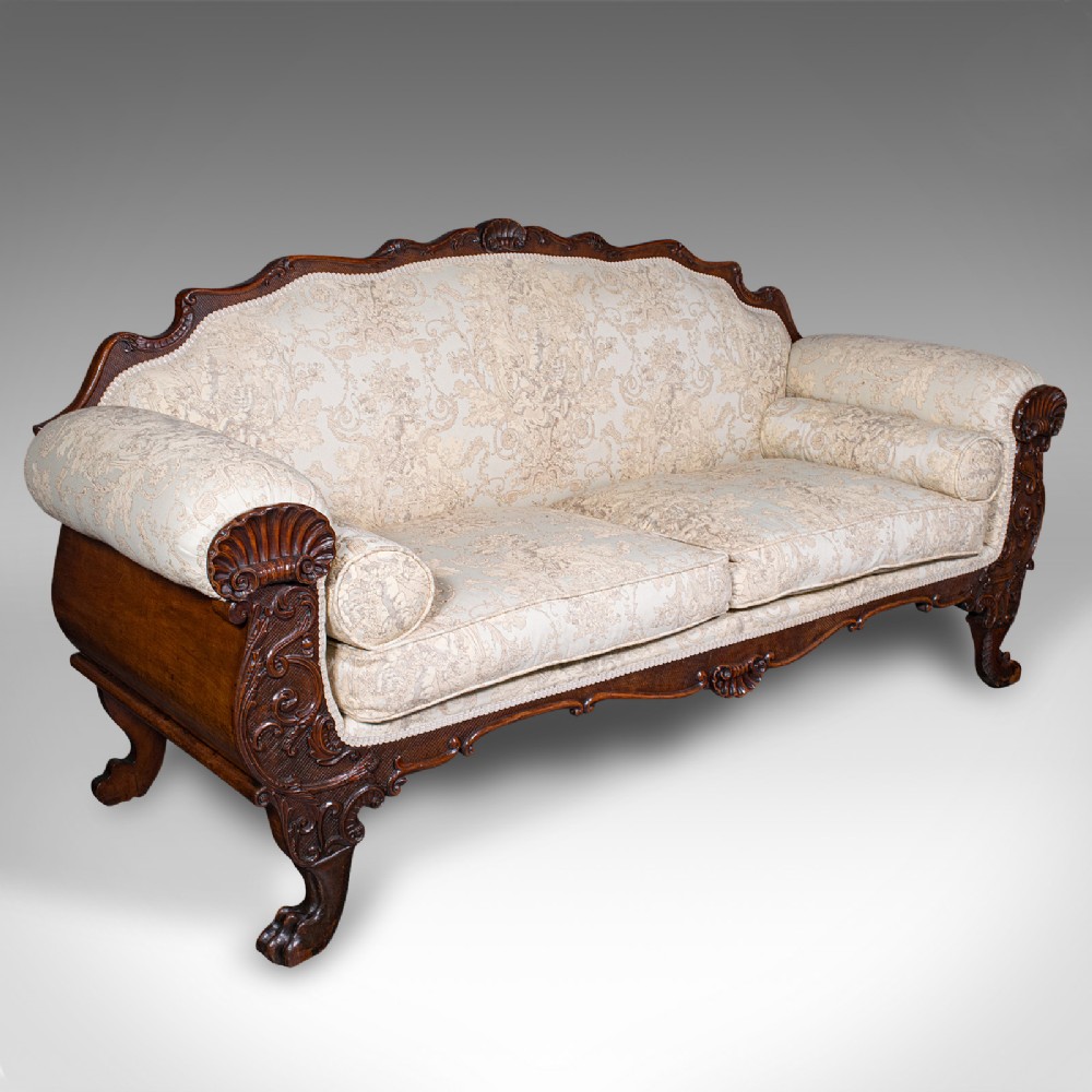 A William IV carved mahogany settee featuring cream patterned damask upholstery, scroll arms, bolster cushions, and detailed paw feet.
