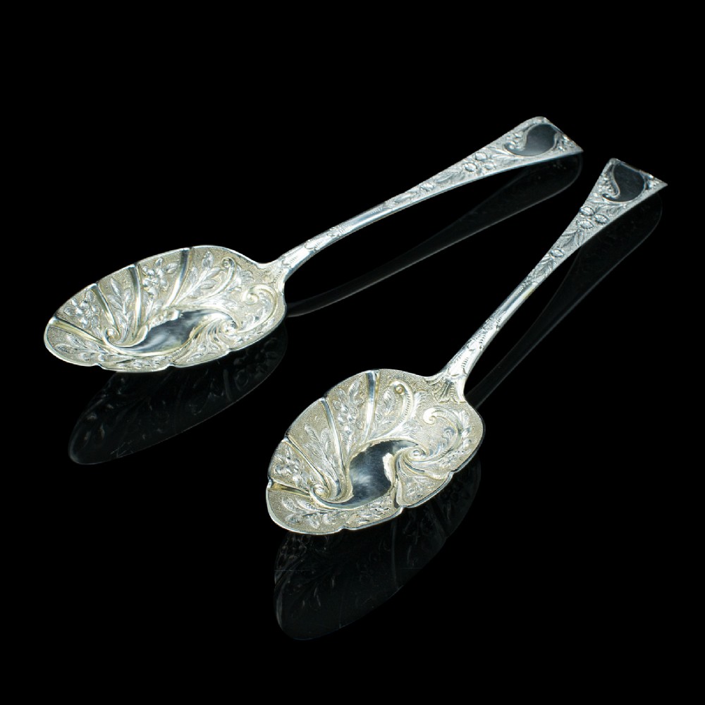 A pair of antique Georgian hallmarked sterling silver dessert spoons with ornate repousse foliage decoration in the bowls and stems.