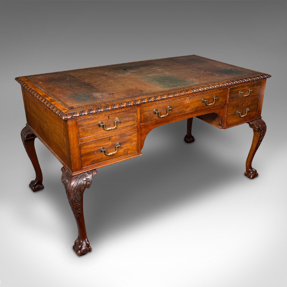 An antique Edwardian mahogany writing desk featuring an inset leather top, carved gadrooned edge, five drawers with brass handles, and cabriole legs terminating in ball and claw feet.