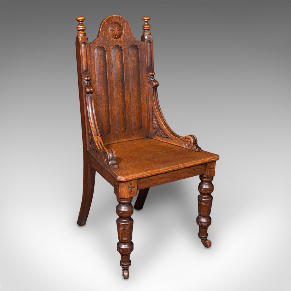 A Victorian Scottish oak Gothic Revival hall chair featuring a carved arched back, turned front legs on castors, and cross motifs on the frame.