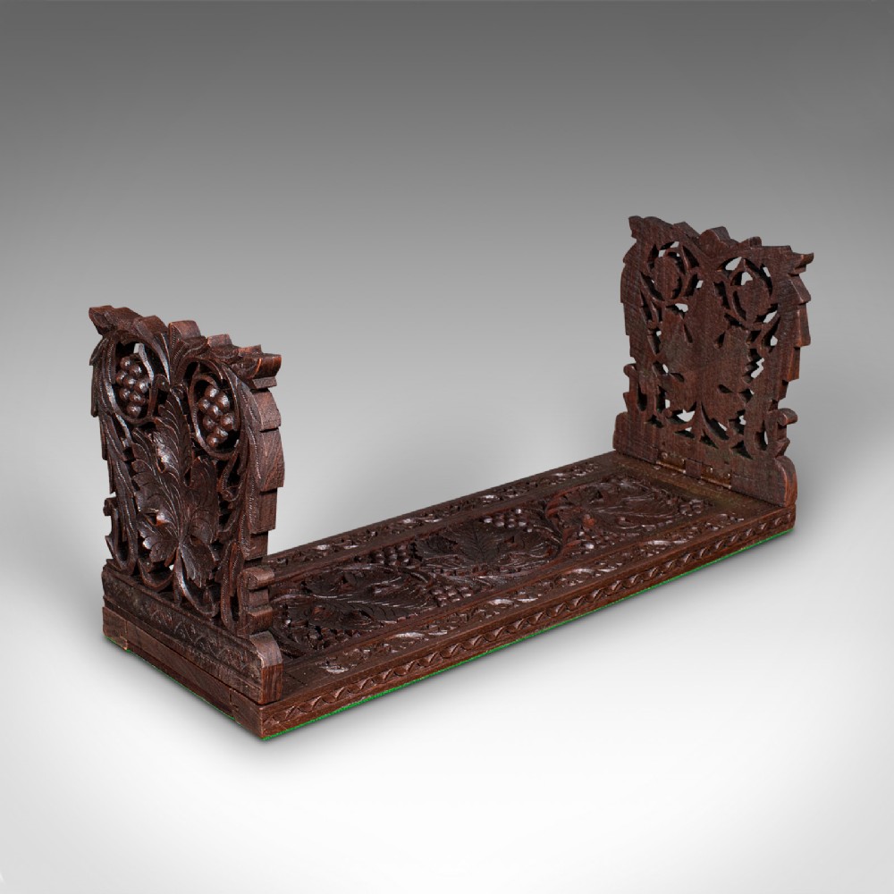 An antique dark carved teak extending book slide featuring floral fretwork foldable ends and a carved base.
