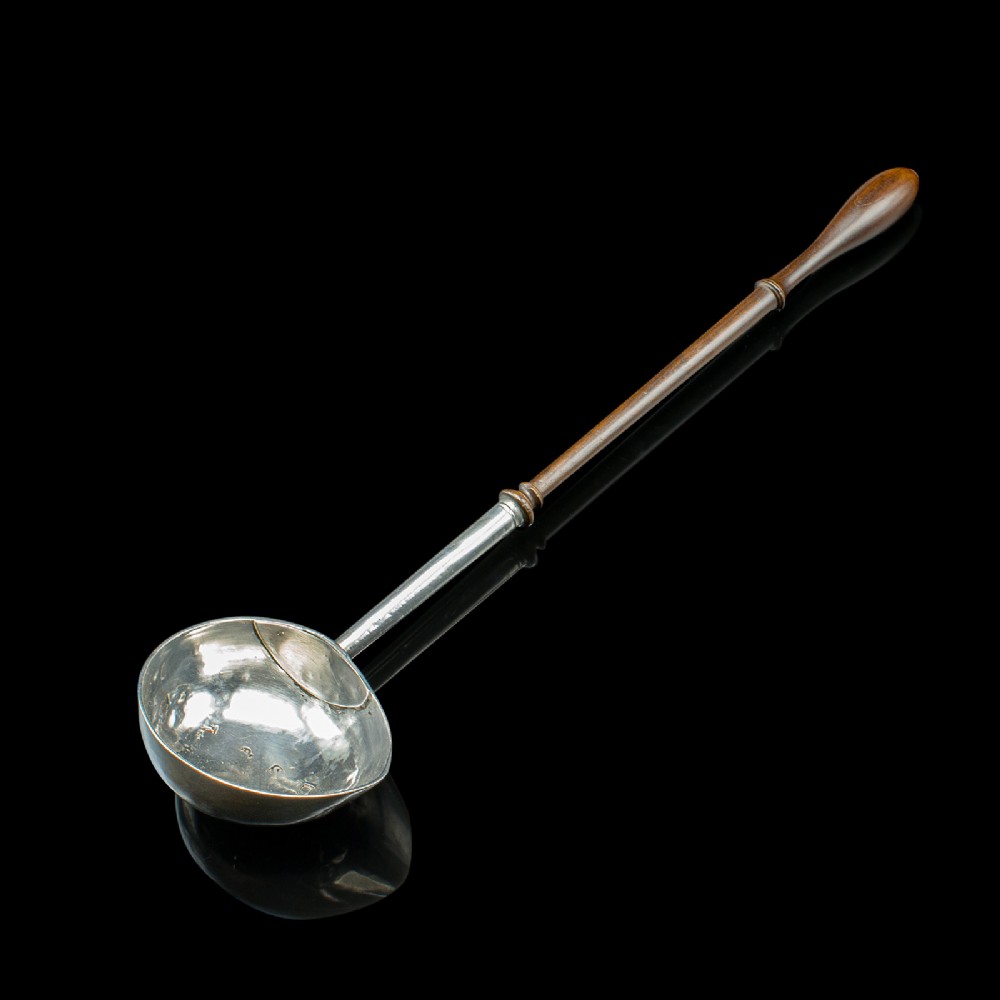 An antique Georgian silver toddy ladle featuring a round bowl with an internal partition and a long turned wooden handle.