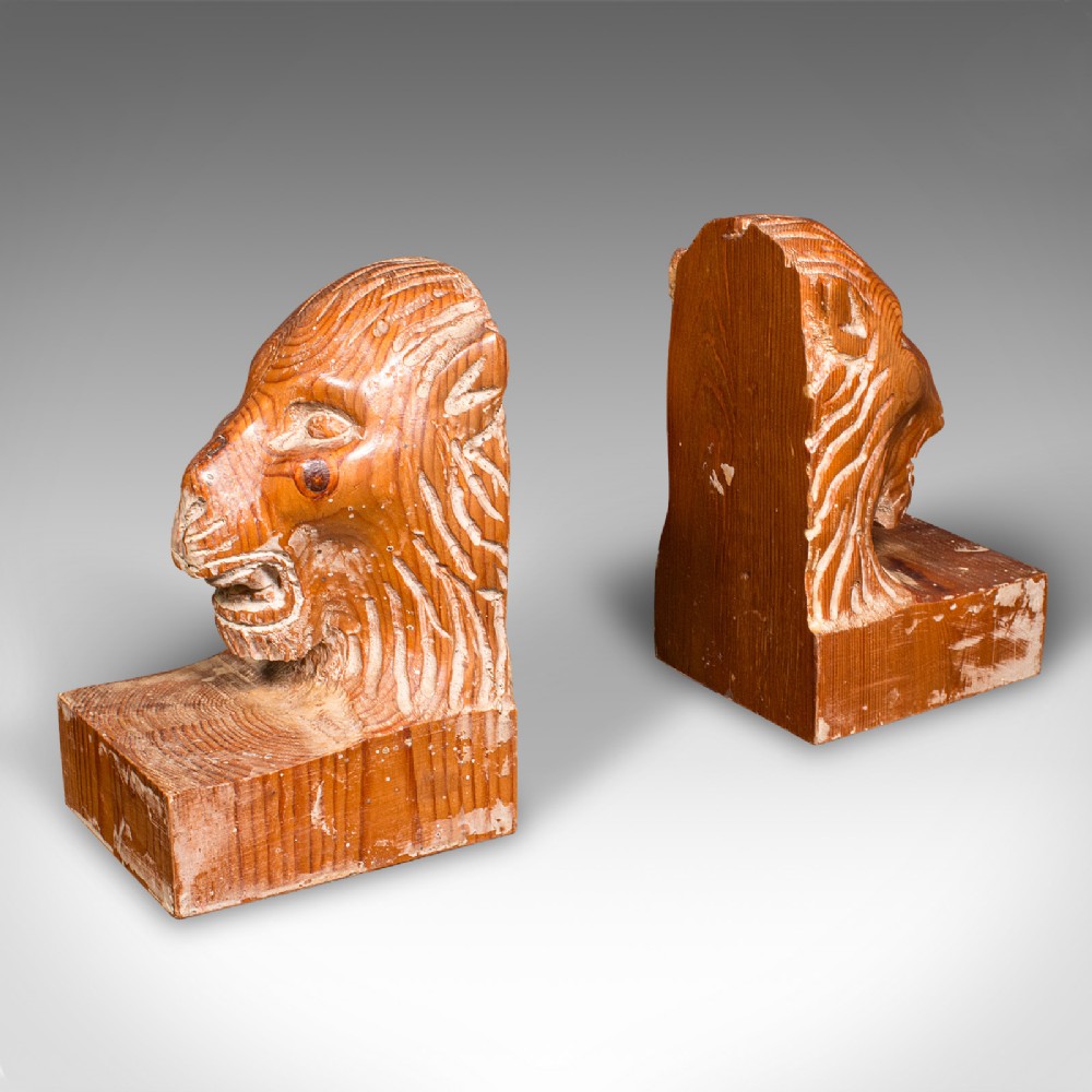 A pair of hand-carved pine bookends featuring lion heads set on rectangular wooden bases with prominent grain details.
