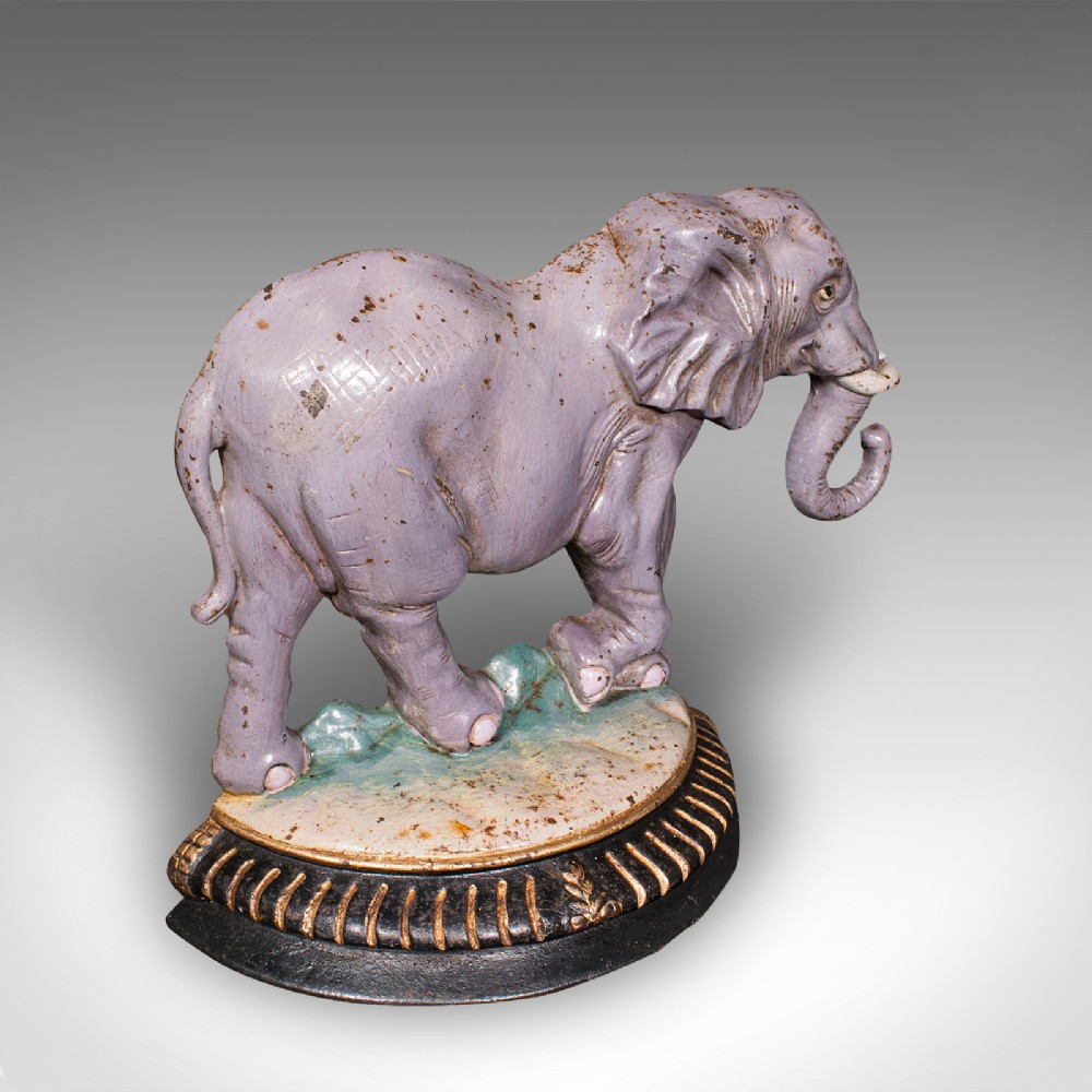 A Victorian cast iron doorstop depicting an elephant with its trunk raised standing on a painted oval base.