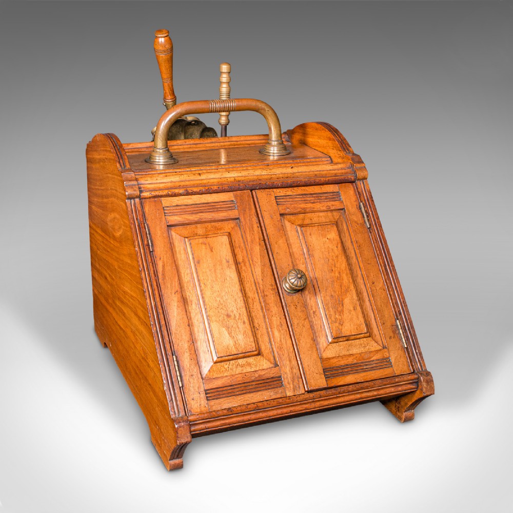 A Victorian walnut coal purdonium with panelled slant-front doors, a brass carrying handle, and an attached shovel mounted at the back.