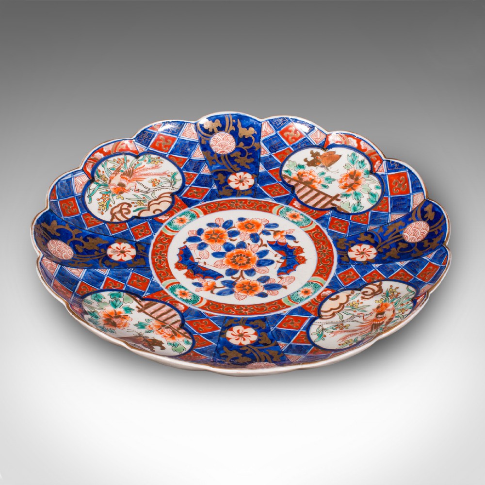 A large circular Japanese Imari porcelain charger featuring a scalloped rim, hand-painted cobalt blue and iron-red floral motifs, and gilded accents.