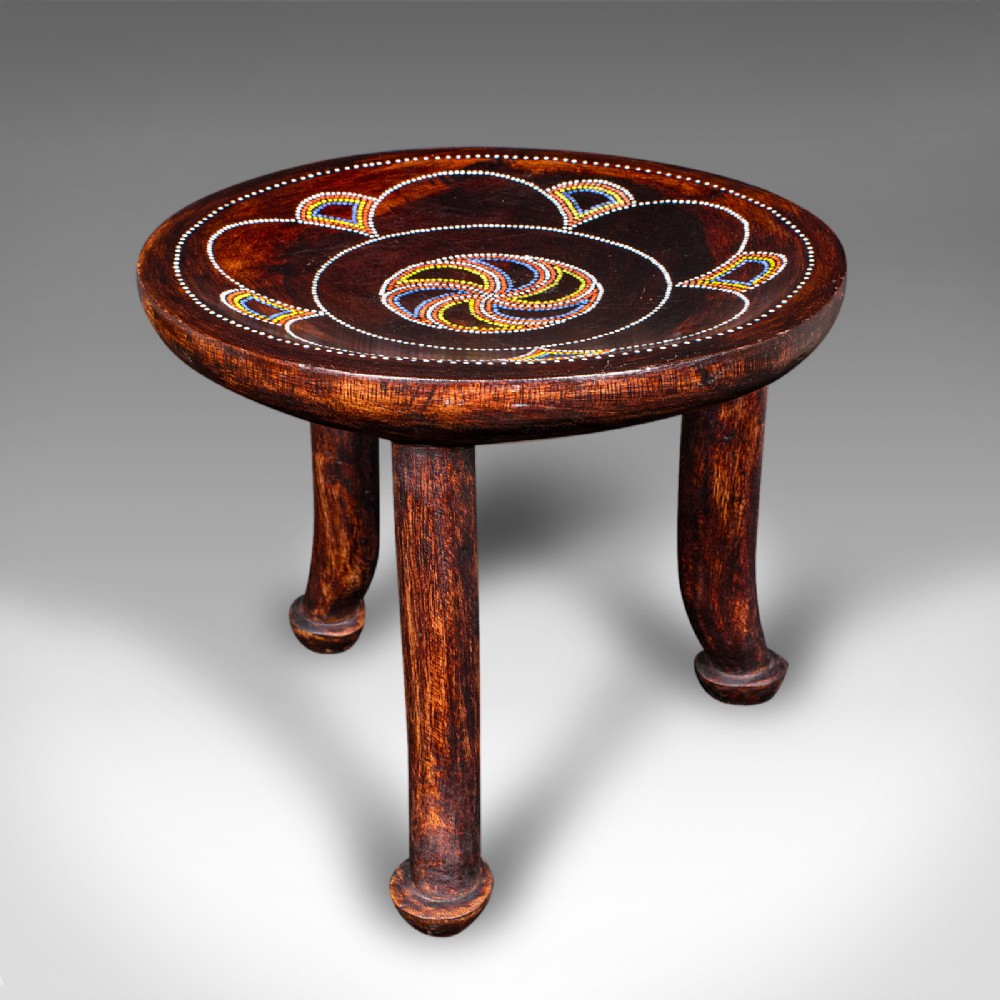 A low circular dark fruitwood side table or stool supported by three splayed legs, decorated with colorful beaded swirl patterns across the top.