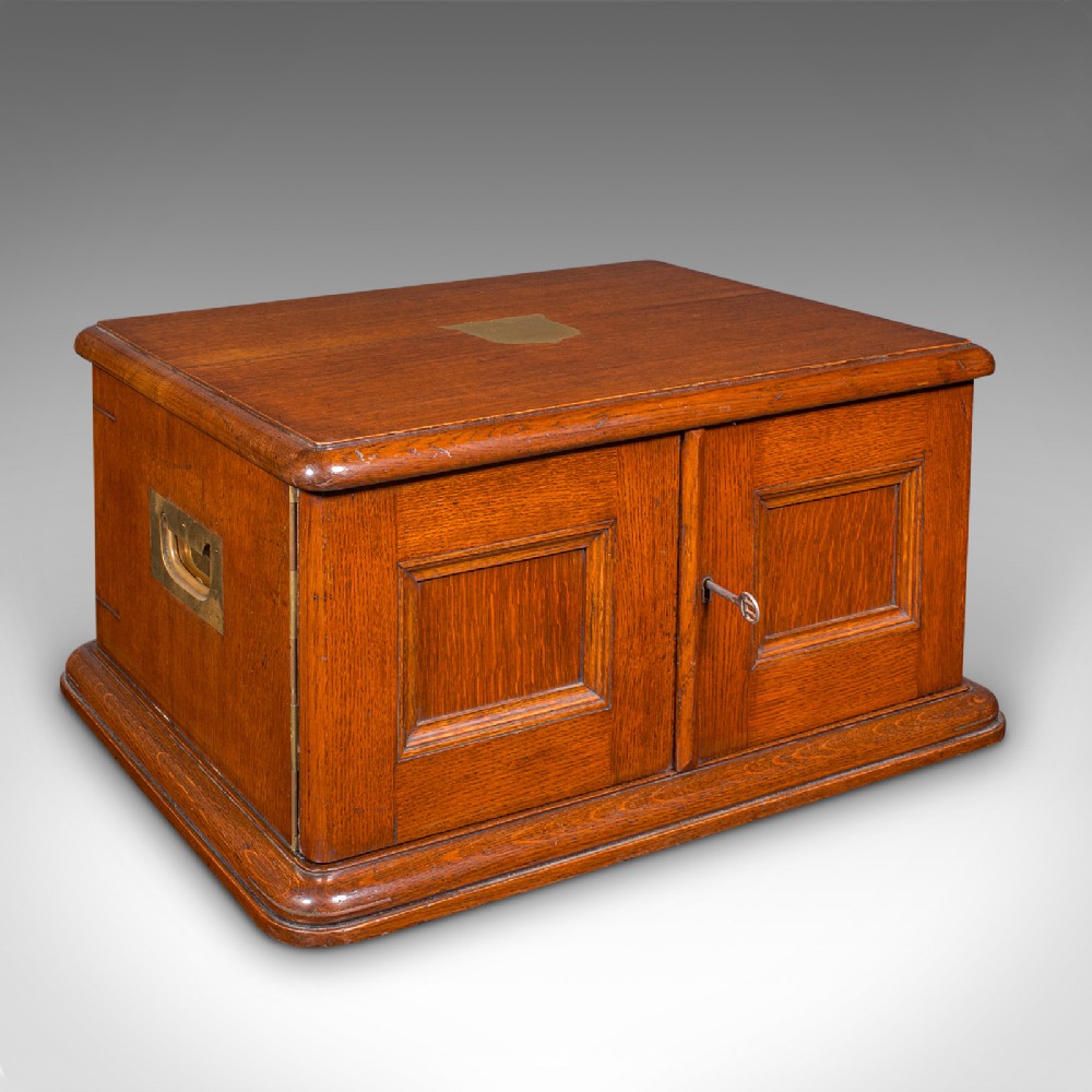 An Edwardian oak cutlery canteen featuring double panelled doors, a central key, side flush brass handles, and a top brass shield cartouche.
