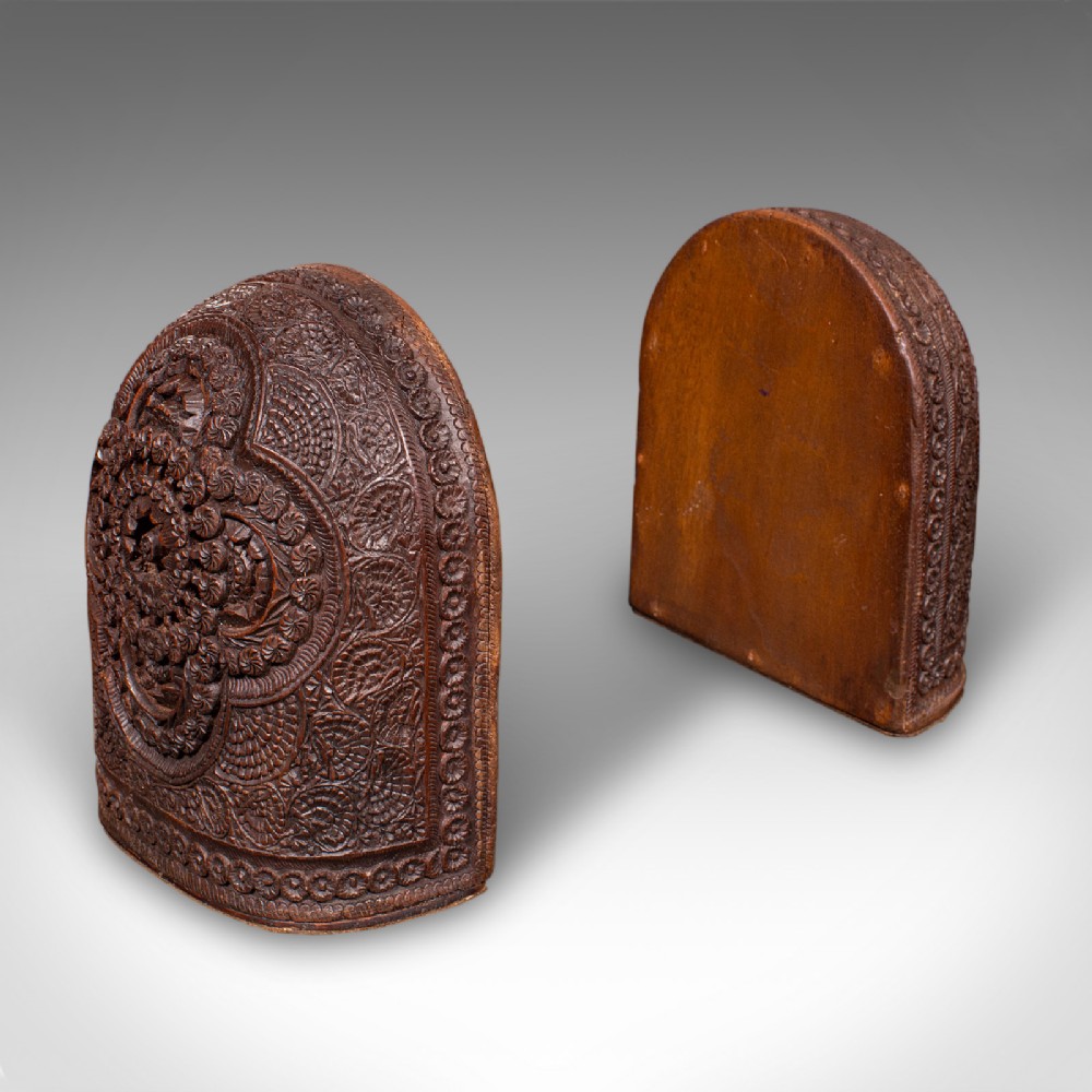A pair of arch-topped antique beech wood bookends decorated with intricate foliate and floral relief carvings.