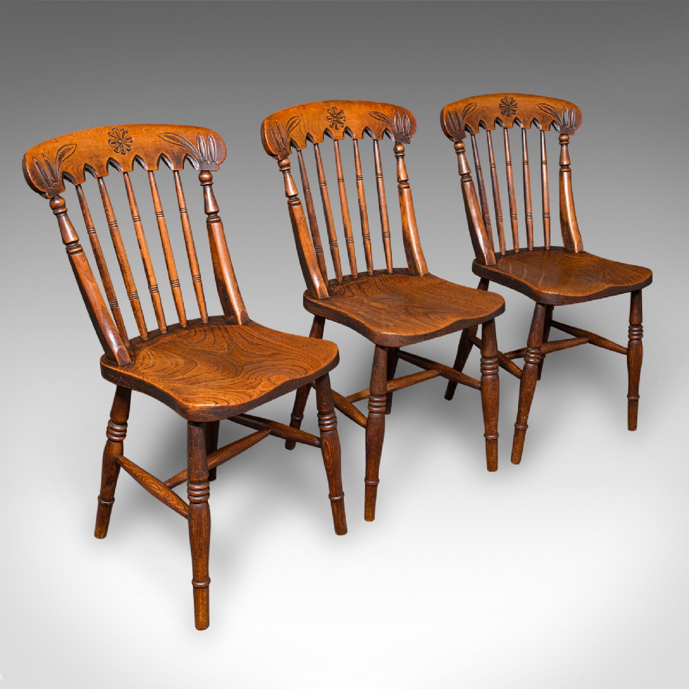 A set of three Victorian wooden side chairs featuring carved backrails, turned spindles, and contoured elm seats.