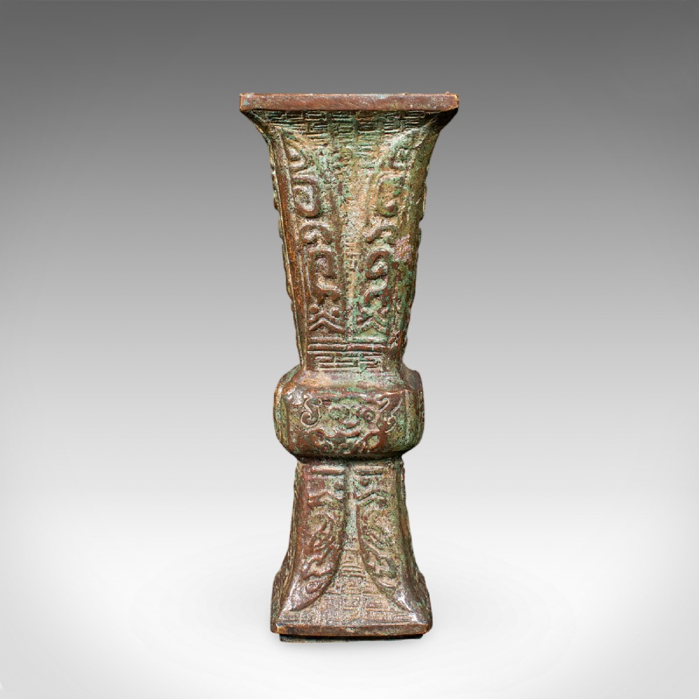 An antique cast bronze Gu ritual vessel featuring a flared rim, central raised knop, archaic relief carving, and verdigris patinated finish.