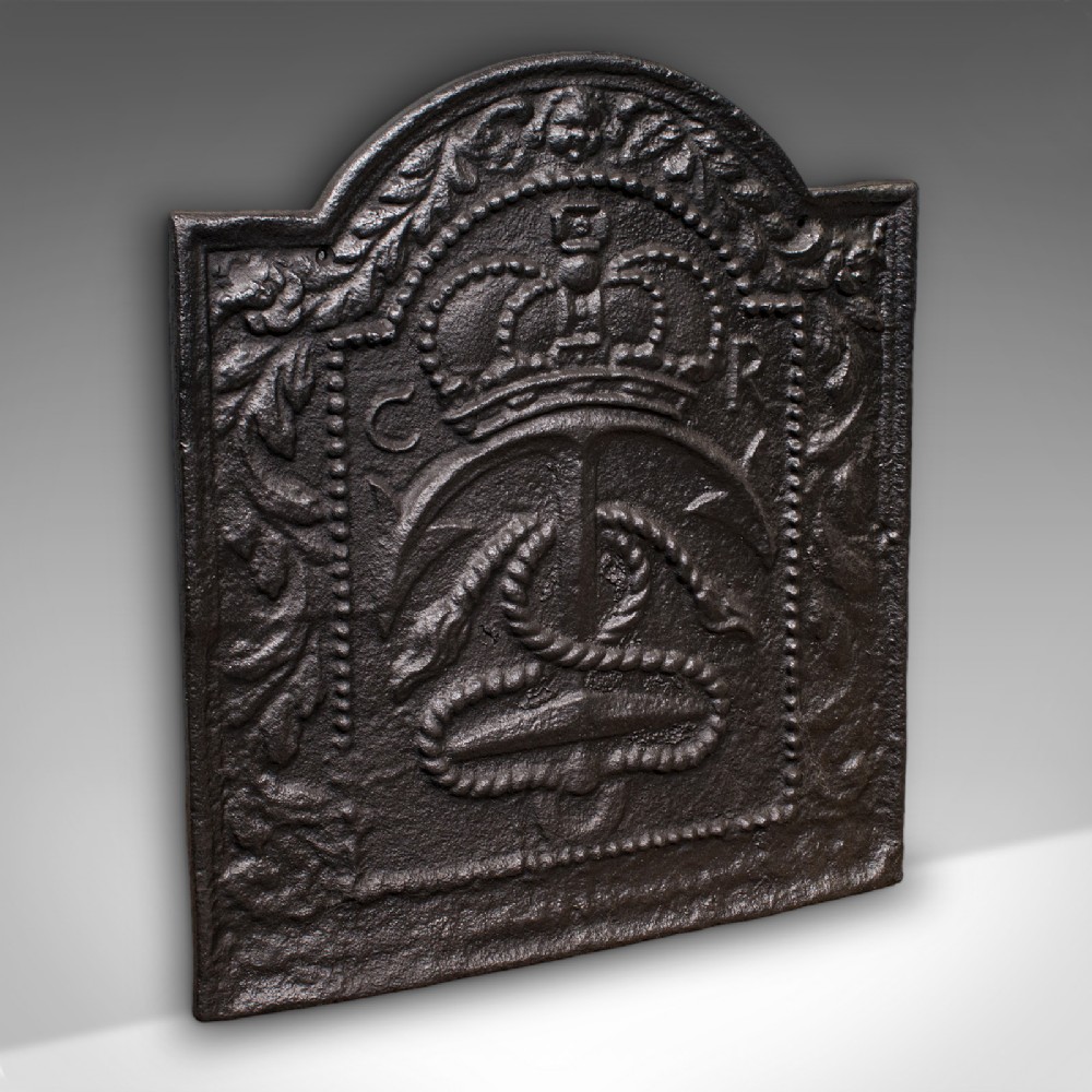 An arched cast iron fire back featuring a raised relief design of a royal crown, an anchor with rope, and foliate borders in a dark patinated finish.