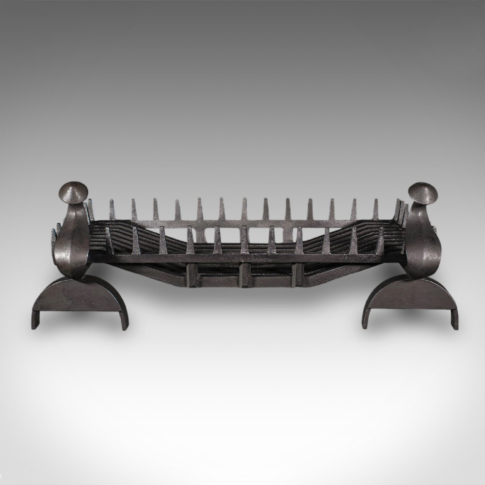 An antique dark charcoal iron fire basket featuring a spiked rail and matching end supports with domed finials on arched feet.