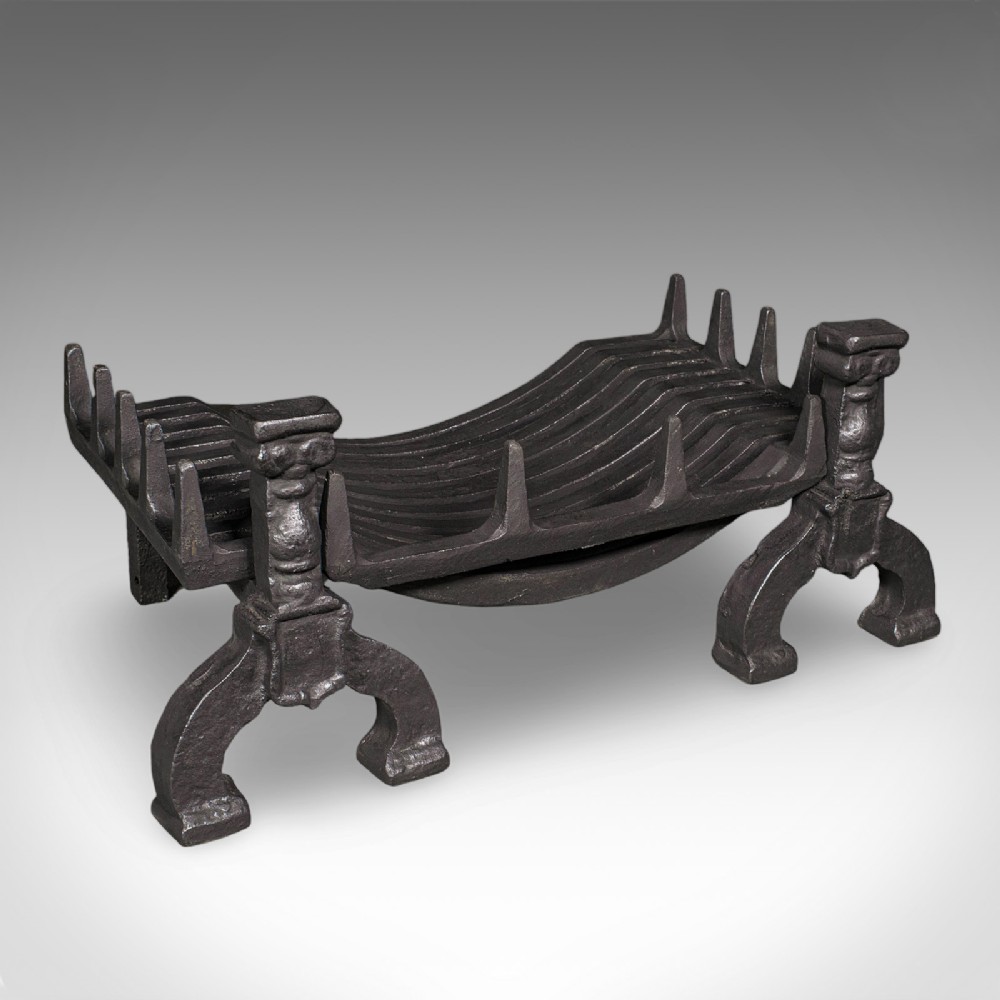 A Victorian cast iron fire basket featuring a slatted cradle resting on decorative firedog supports with baluster columns and curved feet.