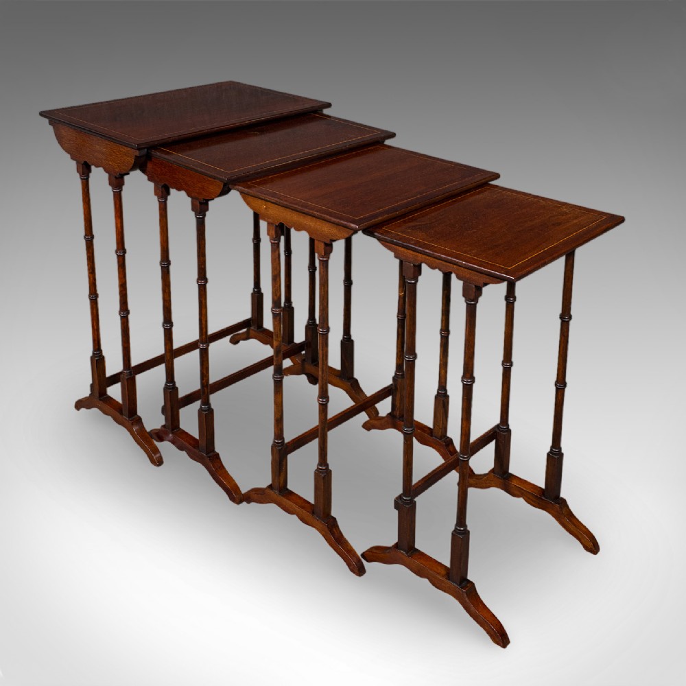 A set of four Edwardian mahogany quartetto nesting tables arranged in a stepped row, featuring delicate turned legs, decorative boxwood inlay, and shaped stretchers.