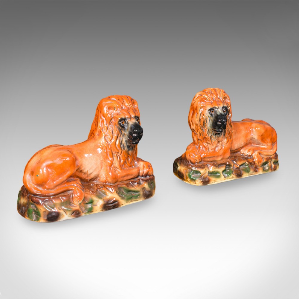 A pair of Victorian glazed ceramic recumbent lion bookends in terracotta orange resting on textured green and brown bases.