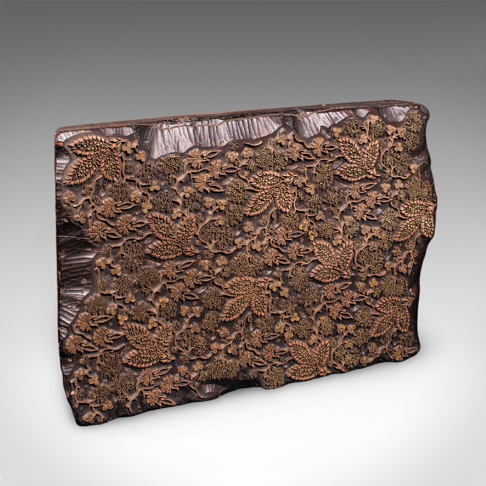 A rectangular dark carved wooden printing block set with intricate brass wire and pin work forming a floral motif.