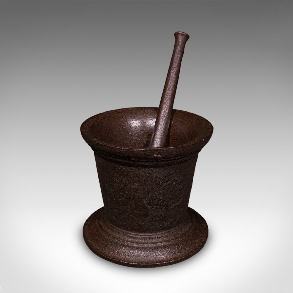 A large Georgian cast iron mortar with a flared rim and stepped pedestal base, accompanied by a solid iron pestle.