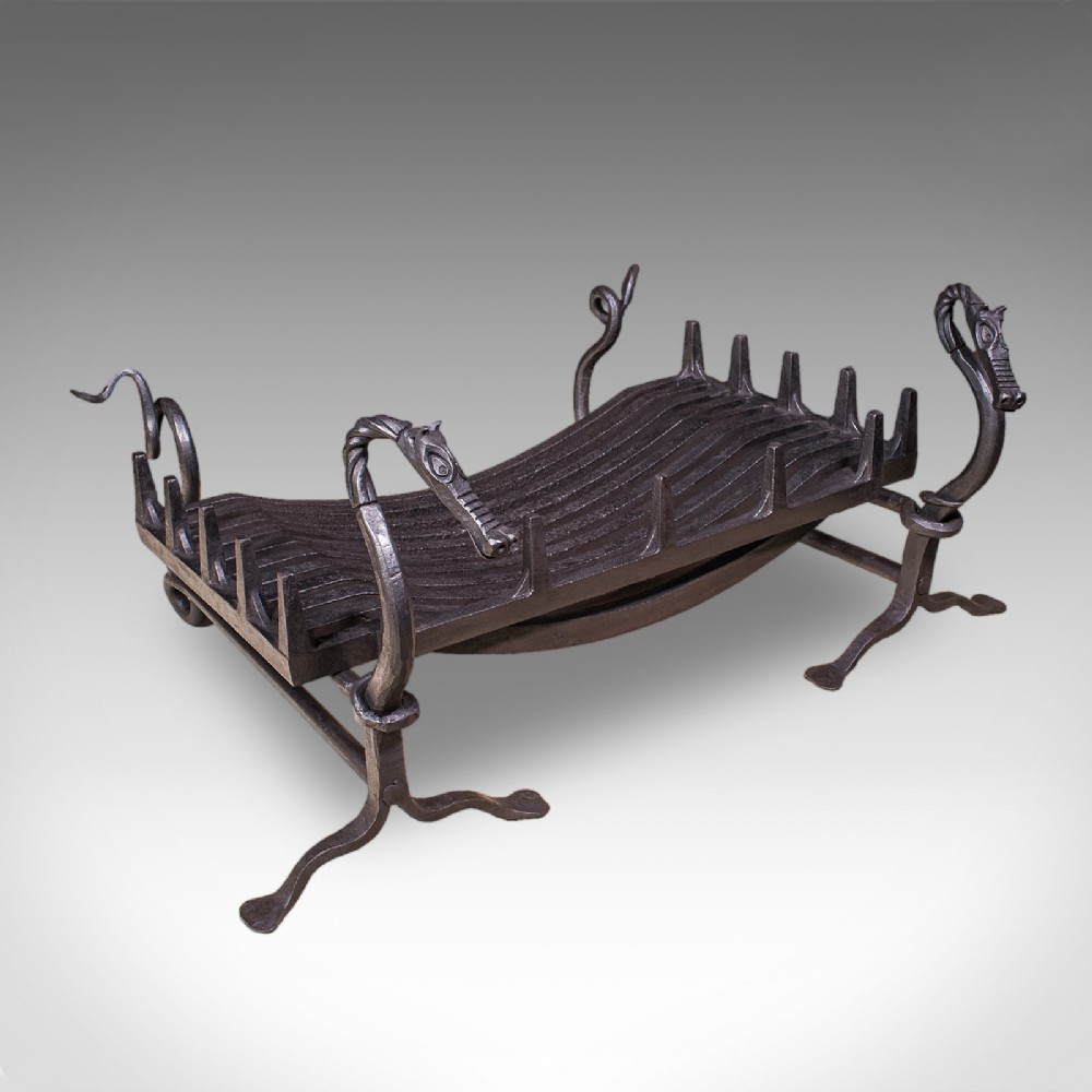A black hand-forged wrought iron fire basket featuring a curved slatted grate supported by four legs with dragon head and tail terminals.