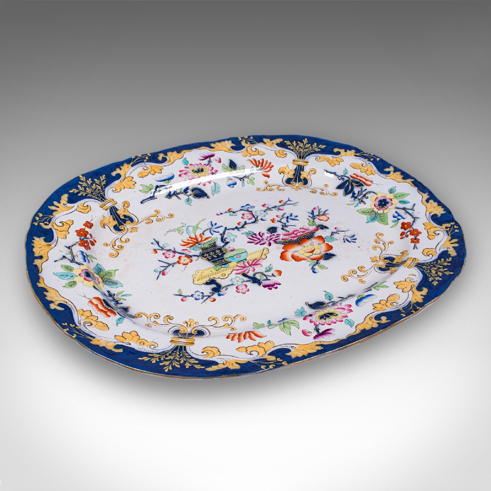 An oval Victorian ceramic meat platter featuring a cobalt blue and yellow scroll border with central polychrome floral motifs.