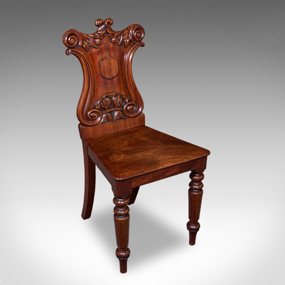 A Victorian mahogany hall chair featuring a relief-carved shield backrest, scroll accents, a solid timber seat, and turned front legs.
