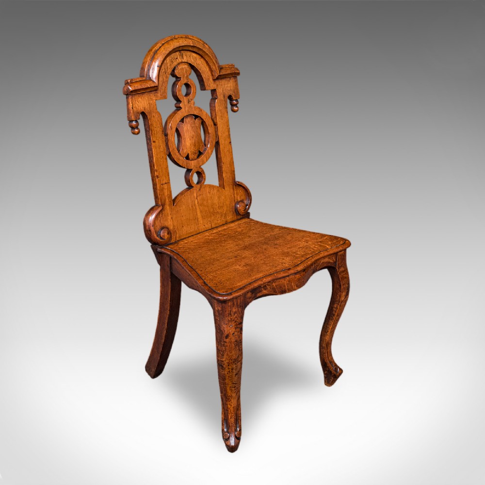 A carved Scottish Victorian oak hall chair featuring a decorative pierced backrest, a solid shaped seat, cabriole front legs, and splayed rear legs.