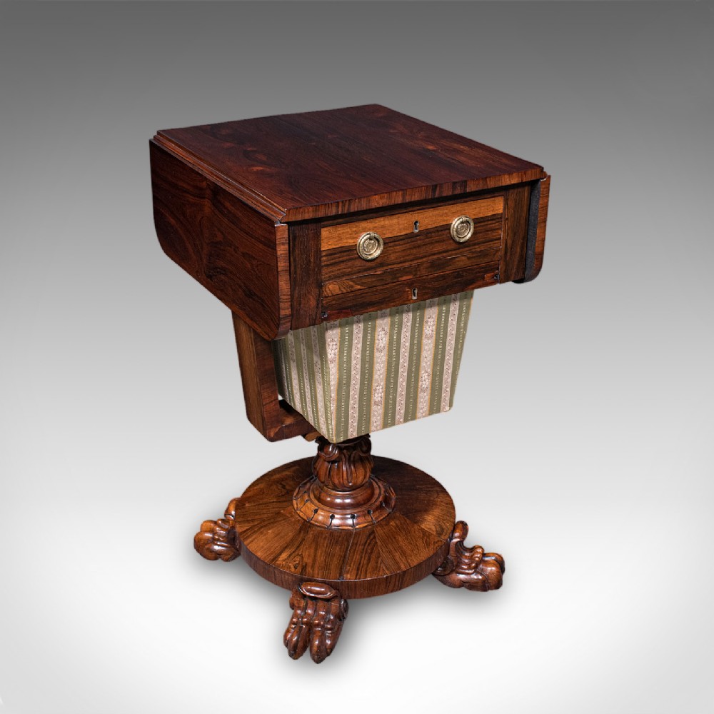 A William IV dark rosewood drop-leaf sewing table featuring a top drawer, a fabric work basket below, and a carved pedestal base with paw feet.