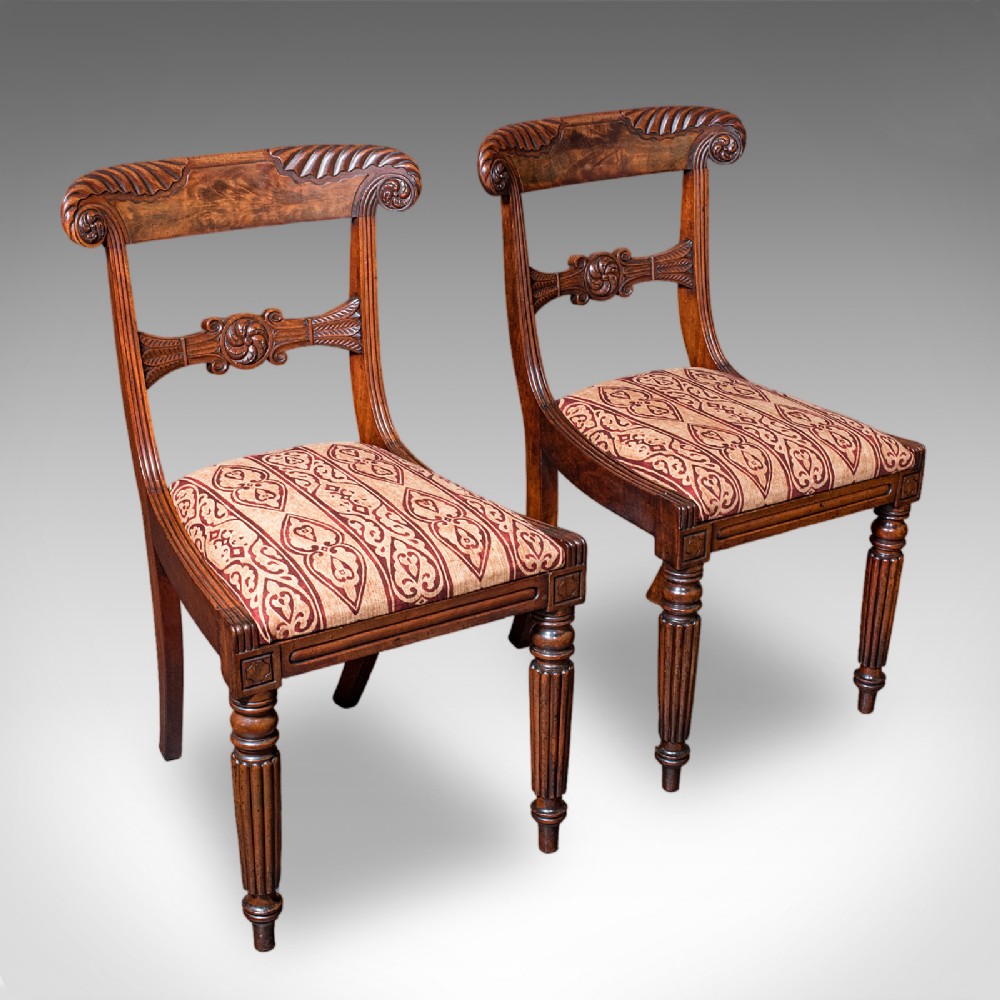 A pair of English William IV mahogany side chairs featuring carved back rails, reeded front legs, and pattern-upholstered seats.