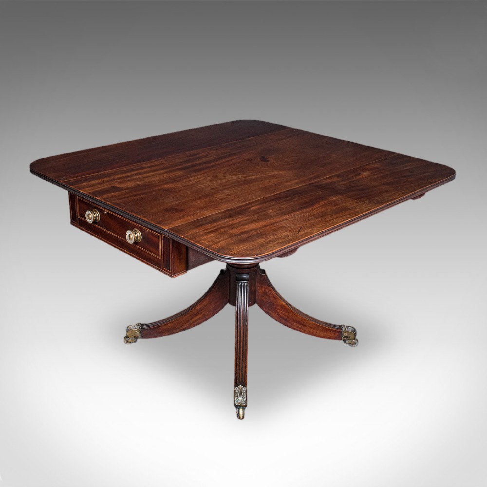 A Regency dark mahogany drop-leaf Pembroke dining table with a central reeded pedestal, four splayed legs with brass castors, and a frieze drawer.