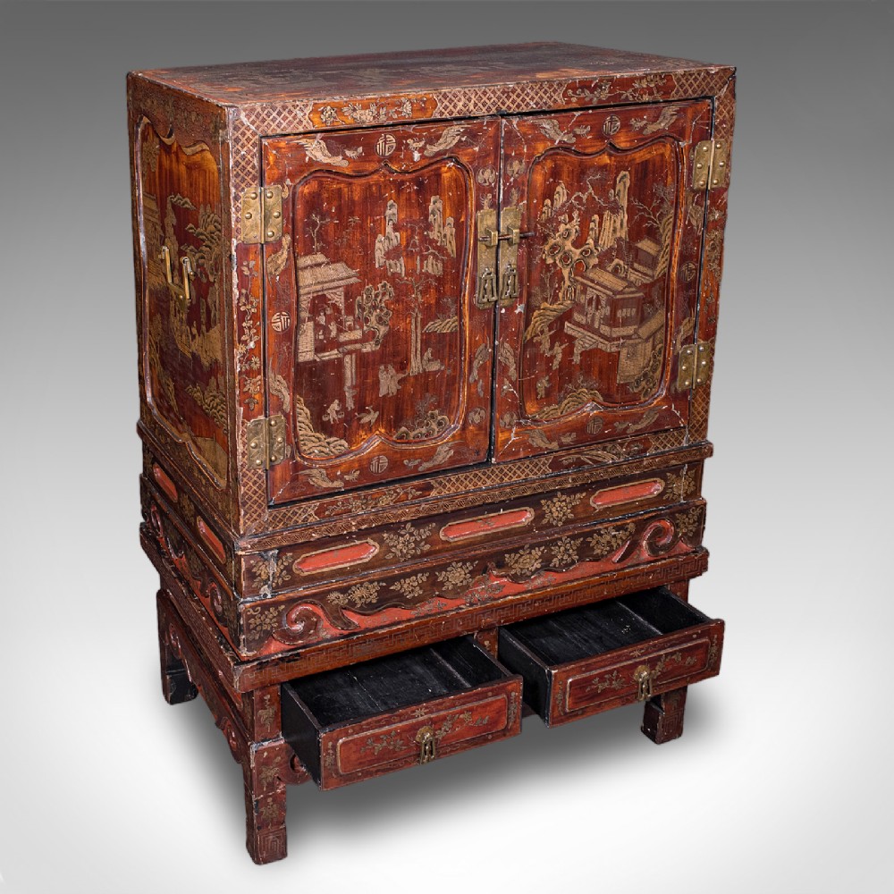 An antique reddish-brown lacquered Chinoiserie campaign cabinet featuring gold gilt landscape scenes, brass corner mounts, and two open lower drawers on a matching stand.
