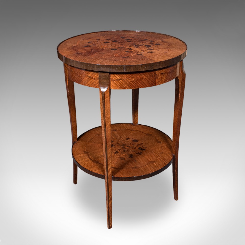 A circular French style two-tier kingwood occasional table featuring intricate floral marquetry inlay on both surfaces and slender tapered legs.