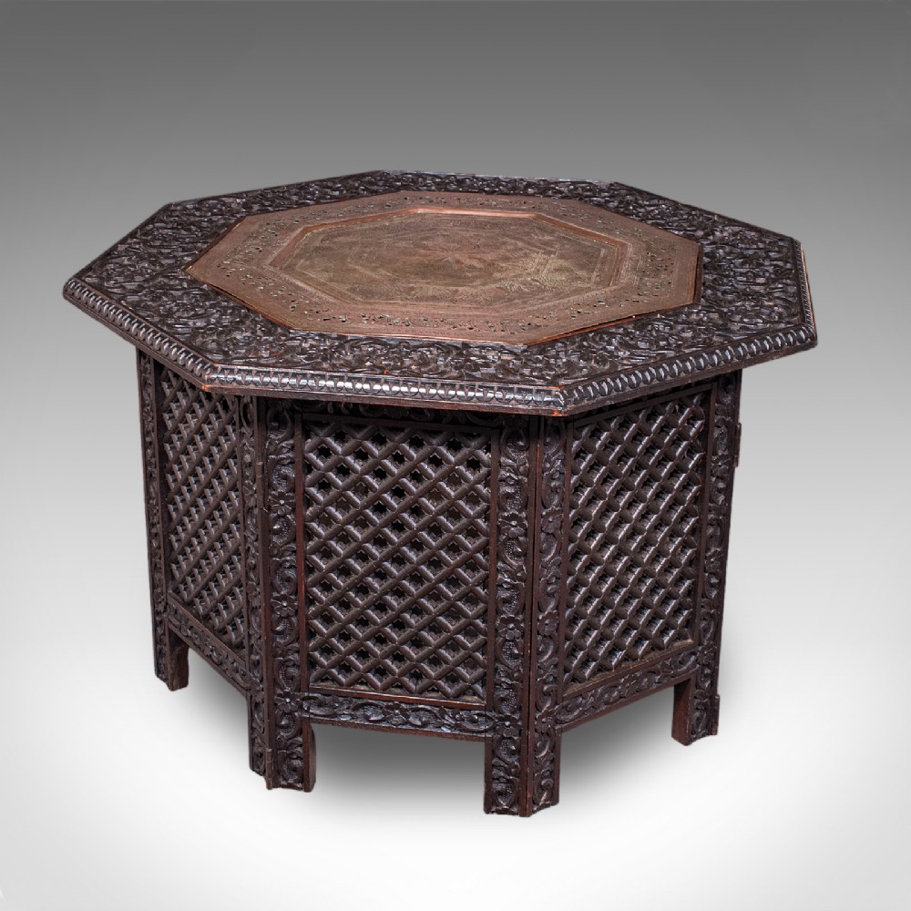 An octagonal dark wood Anglo-Indian tea table featuring deeply carved lattice work side panels and an engraved copper inset top.