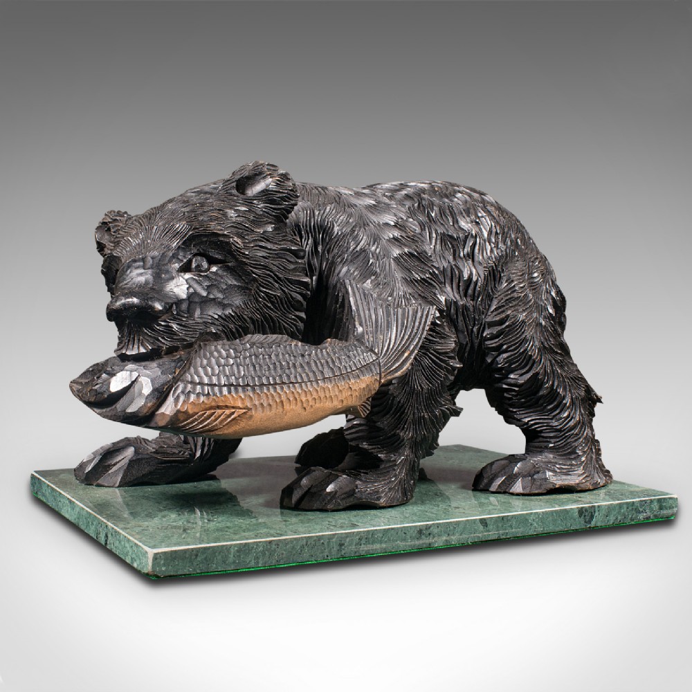 A Japanese carved cedar bear holding a fish in its mouth mounted on a green polished stone base.