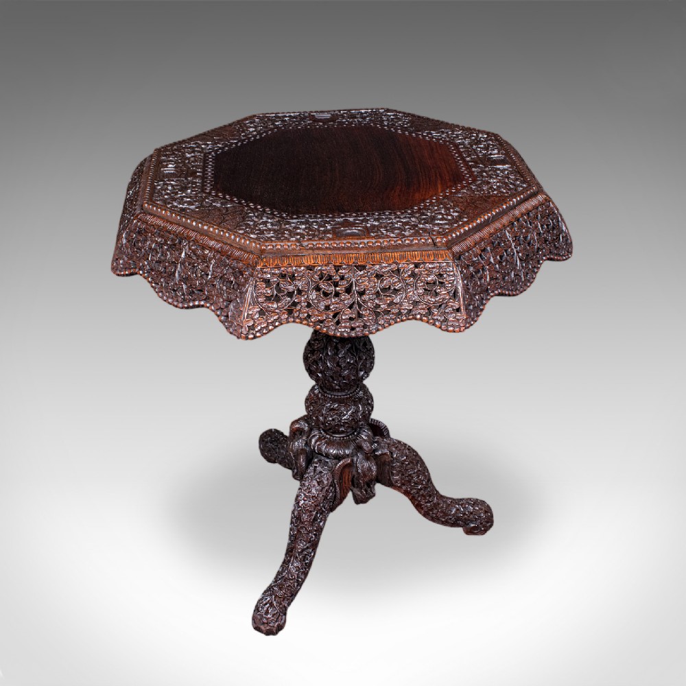 An octagonal Victorian Burmese teak side table featuring intricate relief carving throughout the top apron, central stem, and tripod legs.