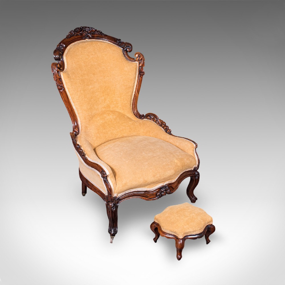 An early Victorian carved mahogany salon armchair upholstered in gold velvet fabric accompanied by a matching small footstool.