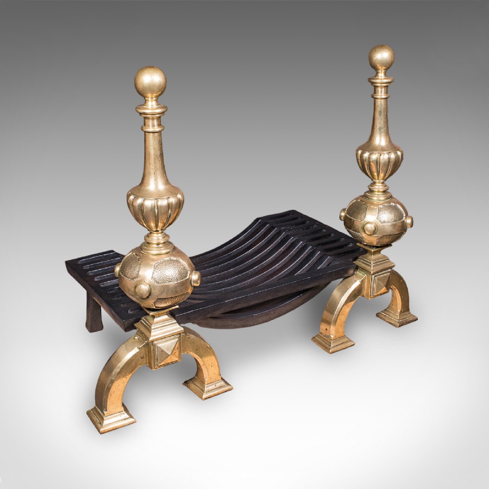A Victorian cast iron fire grate mounted between two tall brass firedogs featuring orb finials and splayed feet.