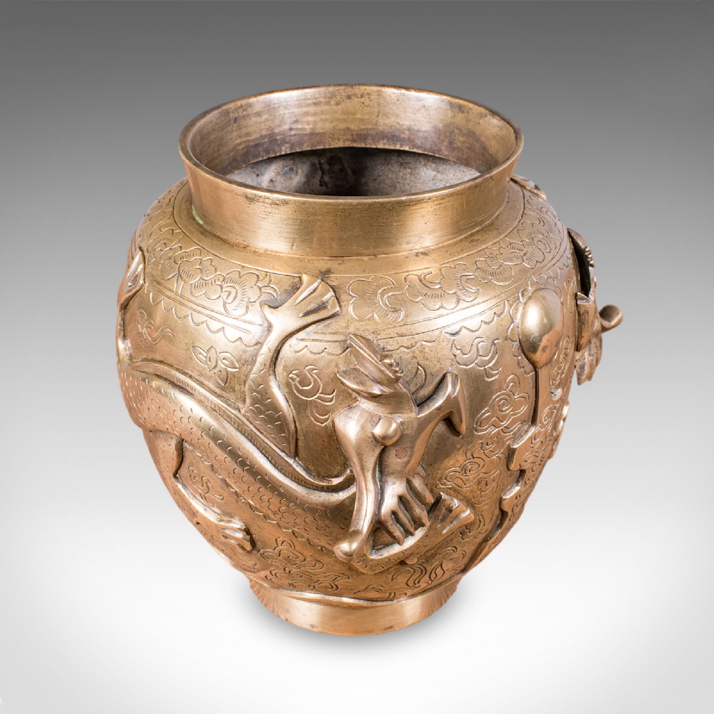 A cast bronze urn featuring a raised dragon motif encircling the body over a chased decorative background.