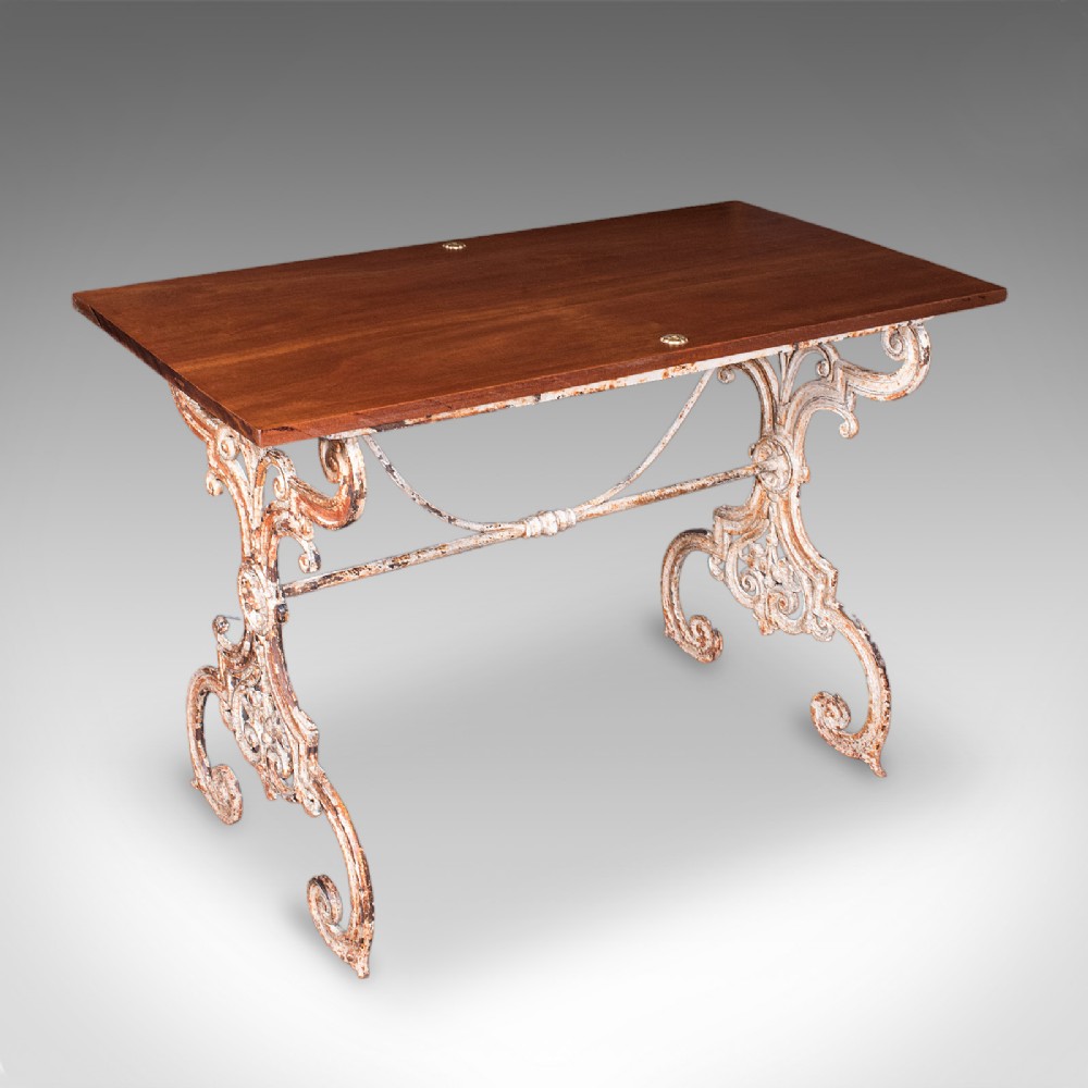 A Victorian table featuring an ornate white distressed cast iron scrollwork base and a smooth mahogany top.