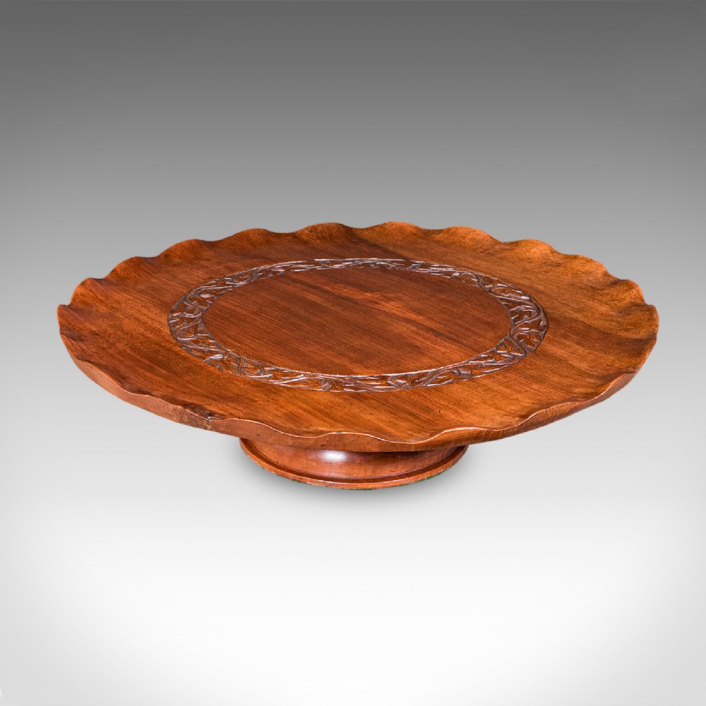 A circular carved wooden lazy susan featuring a scalloped outer border, a central carved foliate ring, and a revolving pedestal base.