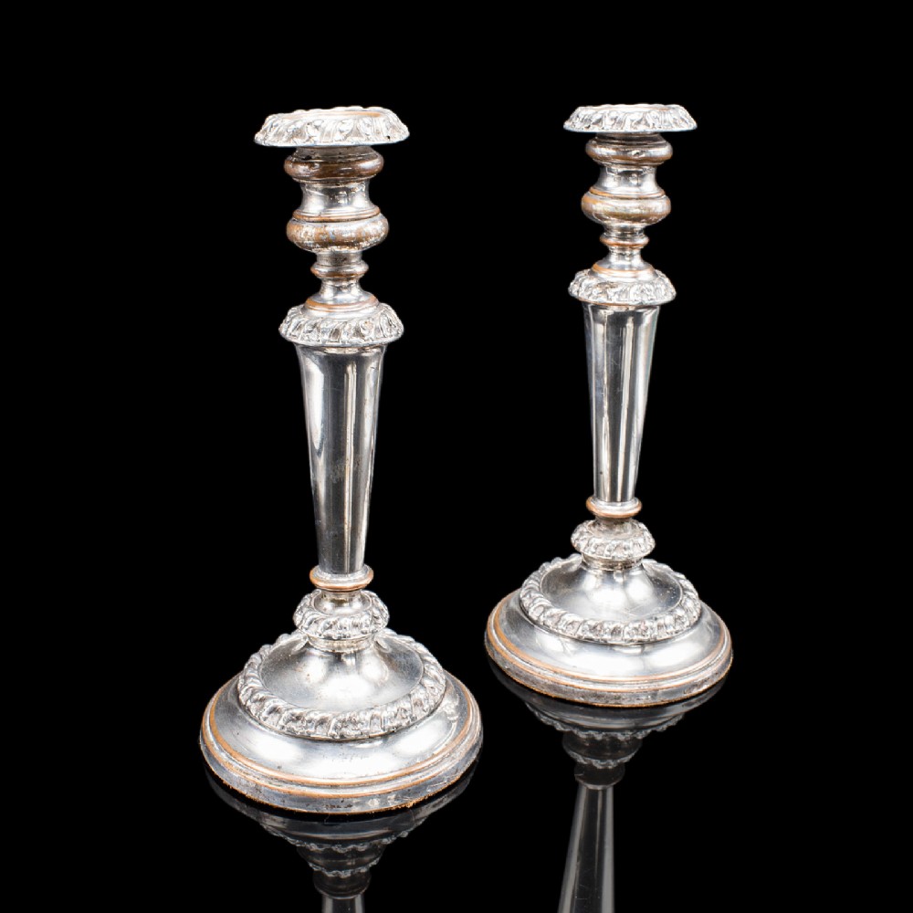 A pair of Regency period Old Sheffield plate silver candlesticks featuring tapered columns, gadrooned borders, and circular bases with copper undertones.
