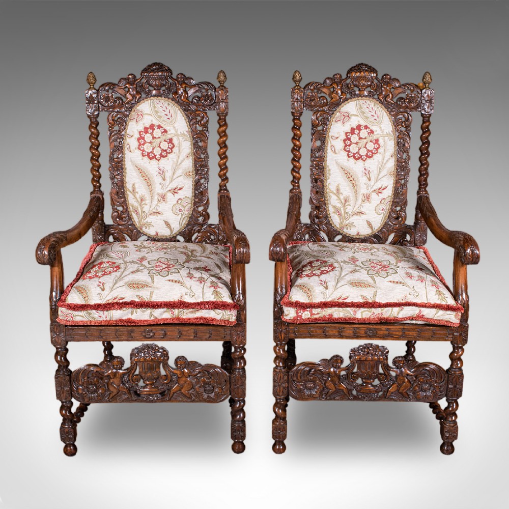A pair of carved dark oak armchairs featuring barley twist uprights, intricate cherub carvings, and cream floral tapestry upholstery with red fringe trim. View III