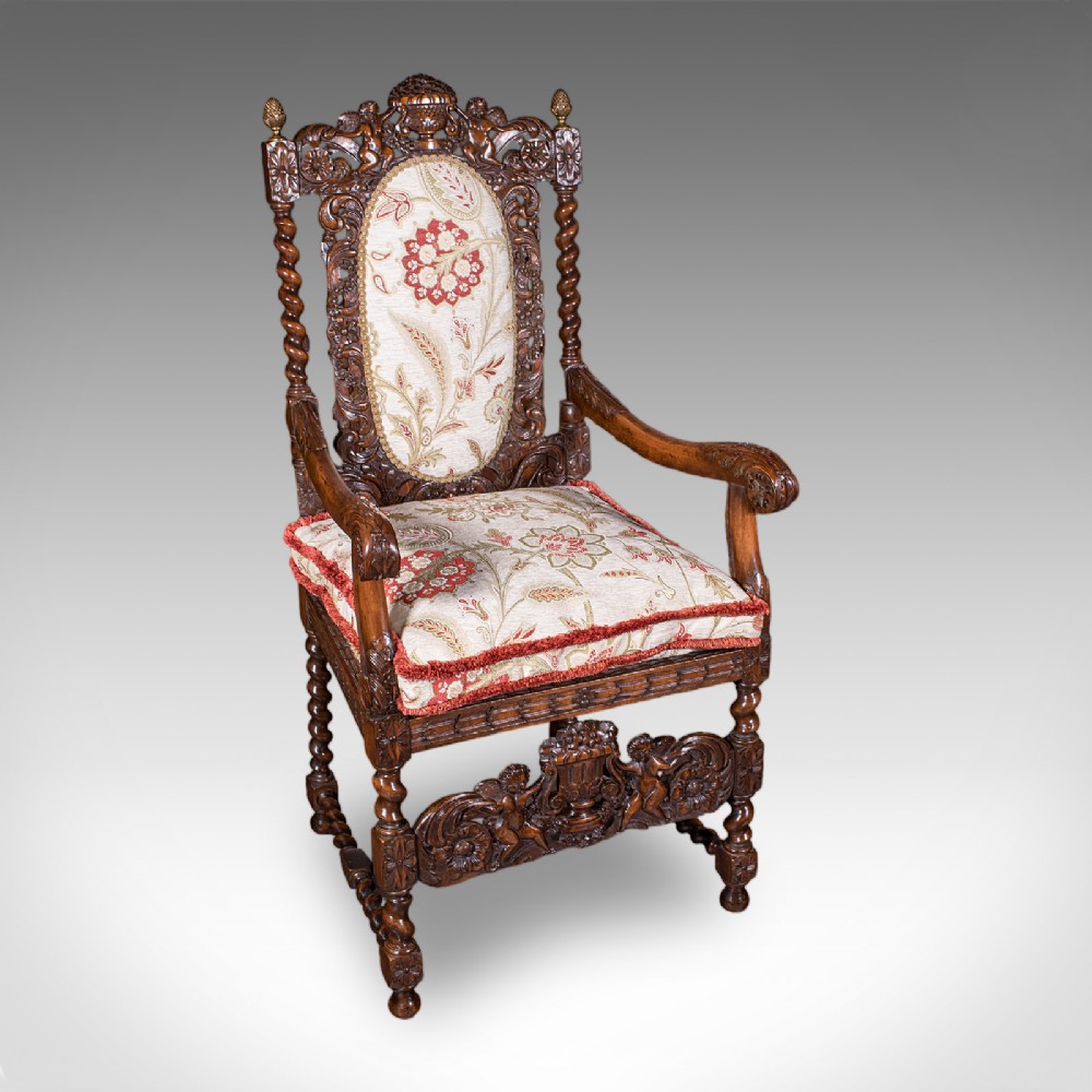 A pair of carved dark oak armchairs featuring barley twist uprights, intricate cherub carvings, and cream floral tapestry upholstery with red fringe trim. View V